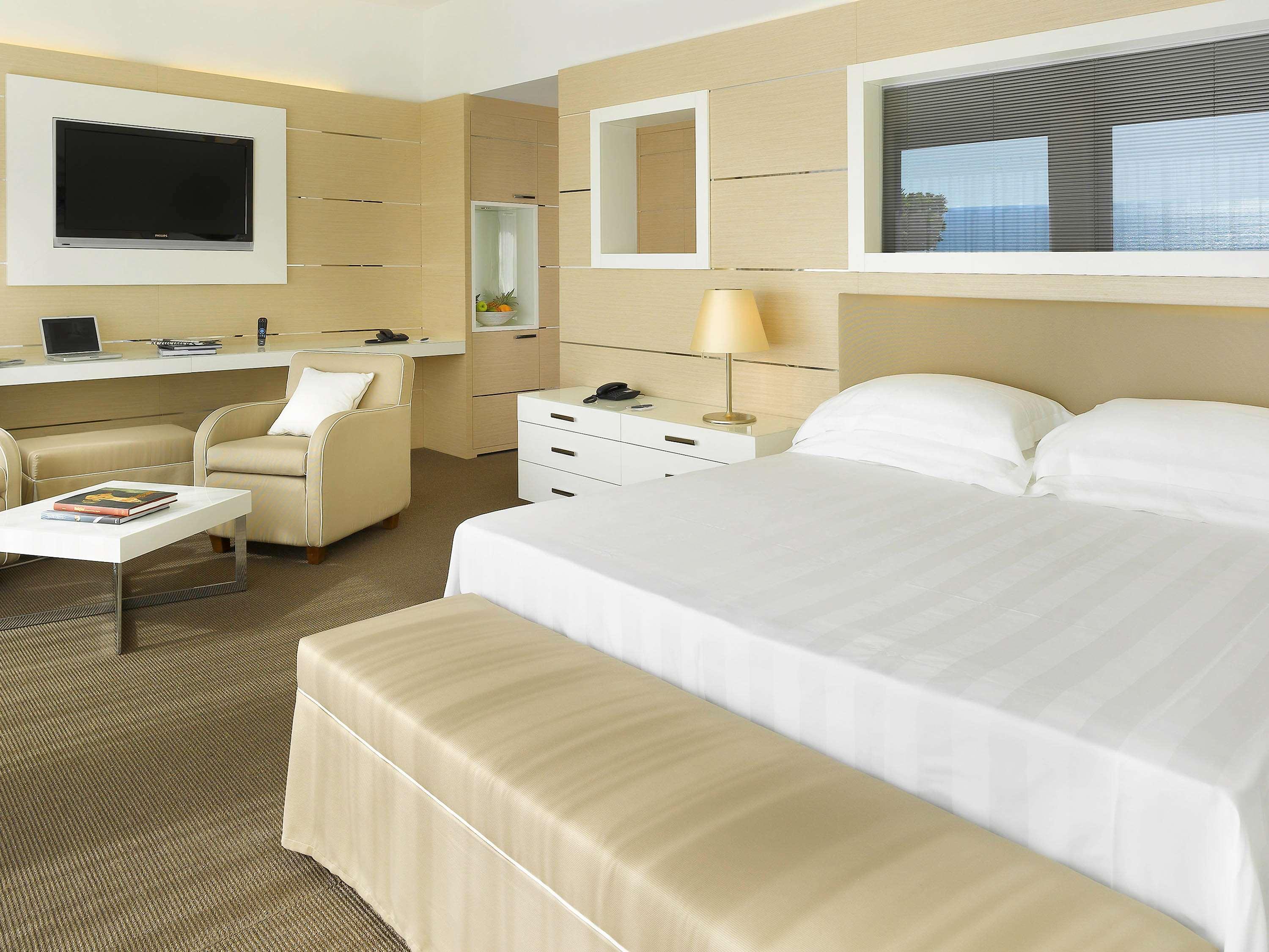Gh Palazzo Suite & Spa Λιβόρνο Εξωτερικό φωτογραφία The photo displays a modern hotel room. It features a comfortable bed with white bedding and pillows. At the foot of the bed, there is a bench with a light-colored cover. To the side, there's a small table with a couple of magazines on it, and a soft