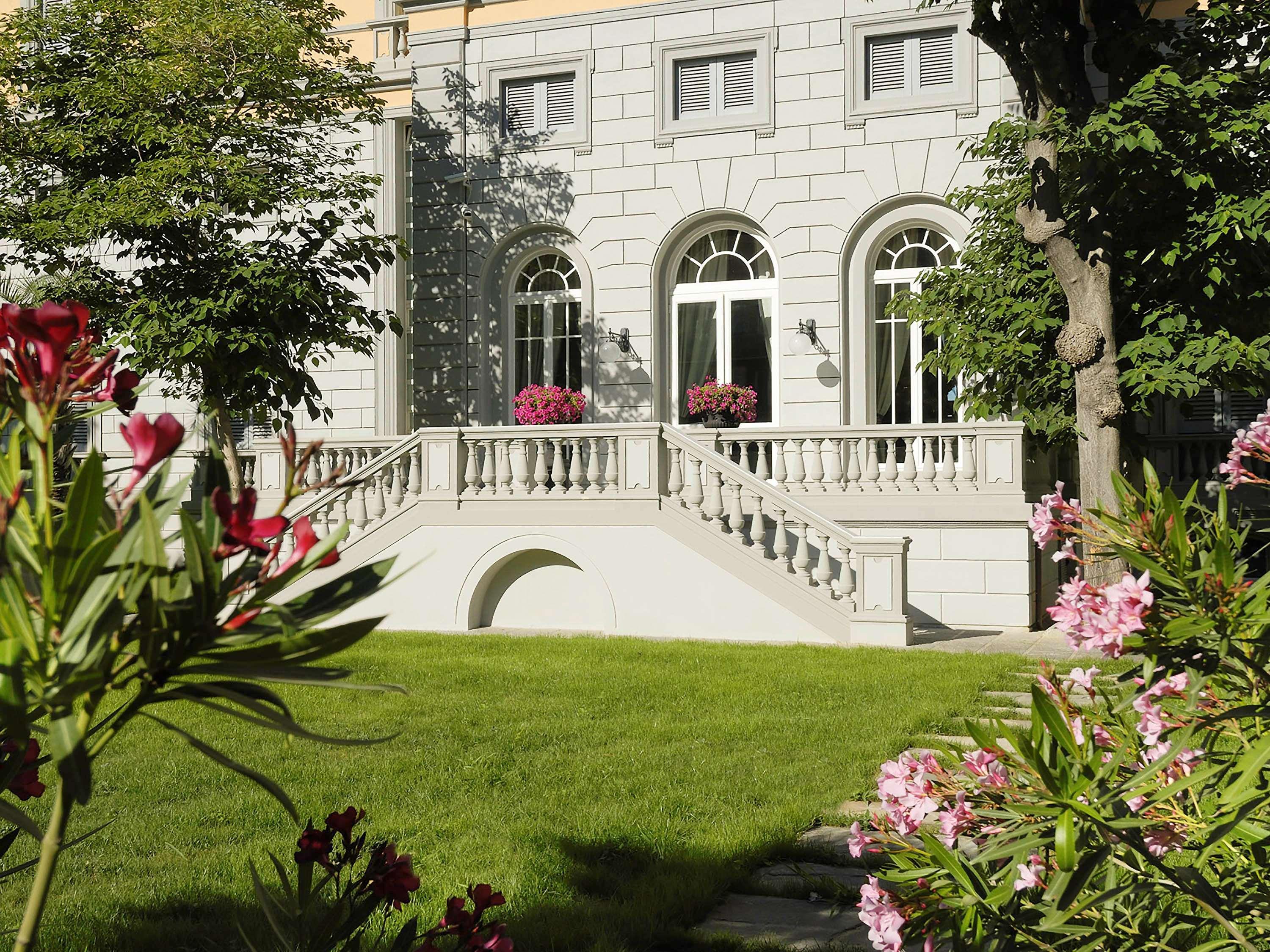 Gh Palazzo Suite & Spa Λιβόρνο Εξωτερικό φωτογραφία The photo shows a beautifully landscaped area featuring a large, elegant building with stone architecture. The building has several large arched windows that allow plenty of light in. A staircase leads up to a terrace with decorative railings. The su